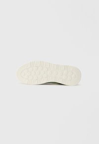 Fehér gumis sneaker talp, körkörös és texturált tapadási mintákkal, lekerekített orral és enyhén megemelt sarokkal a tartósság érdekében.