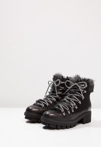 Botas negras hasta el tobillo con ribete de piel sintética, ojales metálicos y cordones grises. Presentan una suela de goma texturizada y un diseño de punta redonda.