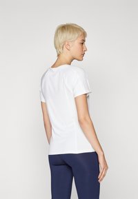 White short-sleeve top with textured side panels, crew neck, and fitted design, paired with navy leggings.