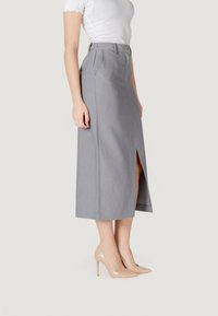 Falda midi gris con una abertura frontal, detalles plisados y una cinturilla ajustada. Combinada con tacones altos color nude. La textura parece suave y bien confeccionada.