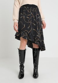 Mustapuku, jossa on korkea-alasu-hemmotus, alareunassa on röyhelö ja kultaisia ja teal-värisiä pyörylöitä. Joustava vyötärö.