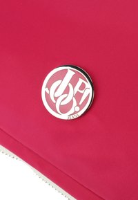 Röd tygväska med en texturerad yta. Har ett runt silverlogo-märke med "JP! JEANS" ingraverat. Dragkedjestängning med dekorativa accenter.