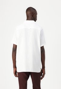 Short-sleeve white linen shirt with a textured finish. Features a classic collar and dropped back hem, viewed from the back on a model.