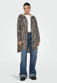 Cappotto a stampa leopardata in tonalità beige e marrone, con cappuccio, chiusura con zip e tessuto leggero. Abbinato a jeans in denim a gamba larga.