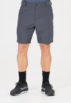 Man draagt donkergrijze knielange shorts, zwarte crew-sokken en zwarte sportschoenen, staand op een witte achtergrond.