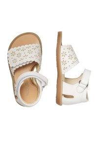 I sandali bianchi presentano ritagli floreali, bordi ondulati e una fascia con fibbia. Realizzati in materiale sintetico con una soletta color cammello e suola in gomma.