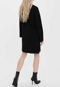 Svart stickad klänning med långa ärmar och sidoöppningar, med en lös passform och en rak silhuett, kombinerad med svarta höga stövlar.