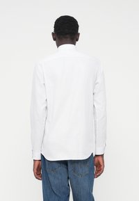 Langärmeliges weißes Hemd mit glatter Textur, Kent-Kragen und geschwungenem Saum, kombiniert mit blauen Jeans aus Denim.