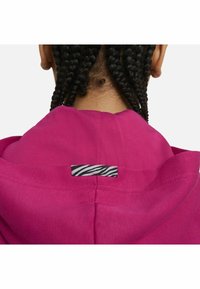 Fuchsia huvtröja i texturerad tyg, med en svartvit zebra-randig etikett på baksidan.