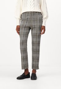 Karierte Hose in Grau und Schwarz mit vertikalen und horizontalen Linien. Slim Fit mit verkürzter Länge, kombiniert mit schwarzen Slippern.