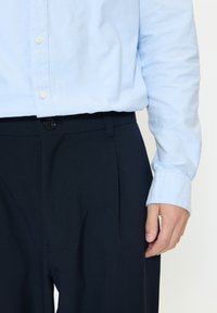 Jasnoniebieska koszula zapinana na guziki o gładkiej fakturze, zestawiona z ciemnogranatowymi spodniami z jednym guzikiem i plisami z przodu.