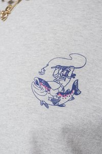 Sudadera gris con una ilustración gráfica de un pescador montando un gran pez, detallada en azul y rosa. Presenta una tela texturizada.