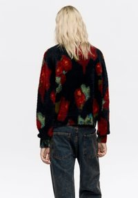 Czarny puszysty sweter z wielokolorowymi kwiatowymi wzorami w kolorach czerwonym, zielonym i niebieskim; noszony z ciemnoniebieskimi dżinsami. Widoczne jasne włosy.