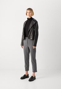 Svart skinnbikerjakke, tettsittende svart genser med høy hals, grå skreddersydde bukser og svarte loafers, som fremhever glatte teksturer og stilrent design.