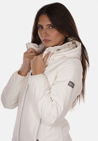 Giacca bianca con zip e colletto alto, caratterizzata da una texture morbida e una patch con logo sulla manica sinistra. Design liscio e aderente.