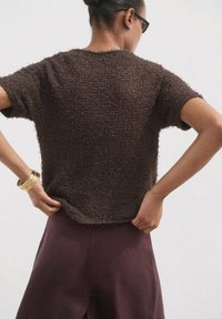 Hnedý textúrovaný top s krátkym rukávom a voľným strihom, vyrobený z mäkkej, plyšovej látky s okrúhlym výstrihom, v kombinácii s tmavo fialovými nohavicami.
