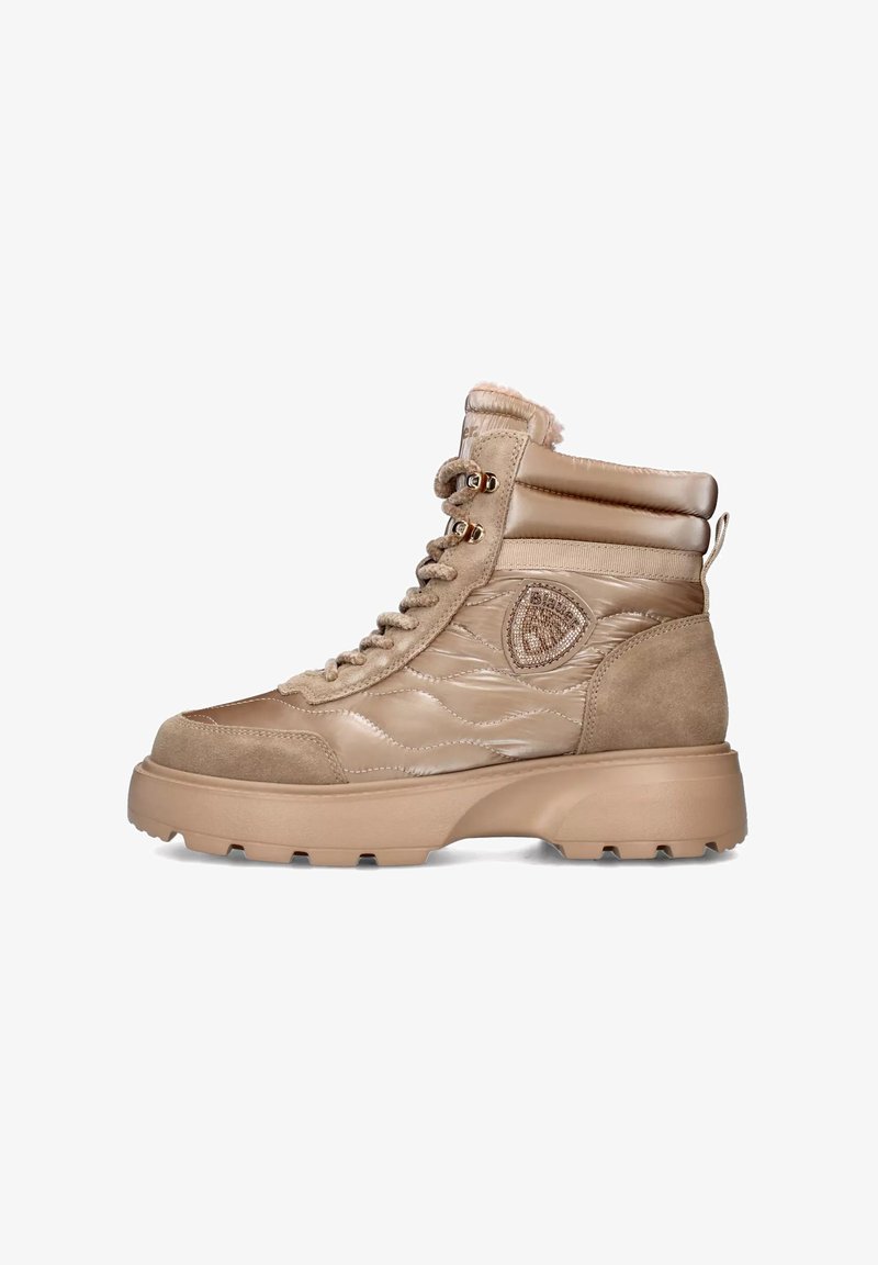 Bottines imperméables beige avec tige rembourrée, accents en daim, garnitures dorées, et semelle épaisse en caoutchouc. Dotées d'un patch logo sur le côté.