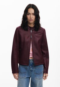 Burgundy leather jacket with a front zip closure, buttoned collar, and seam detailing. Worn over a pink top and paired with blue denim jeans.