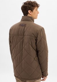 Veste matelassée marron avec un col haut, dotée d'une étiquette en cuir à l'arrière et d'accents boutonnés près de l'ourlet.