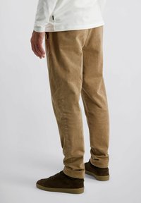 Lichte bruine corduroy broek met verticale ribbels, tapered fit, zijzakken en gecombineerd met donkerbruine sneakers.