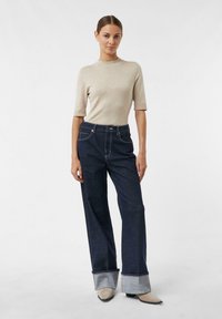 Jasnobeżowy krótki sweter z krótkim rękawem w połączeniu z wysokim stanem, ciemnoniebieskie spodnie dżinsowe o szerokich mankietach i jasnoniebieskim wnętrzu.