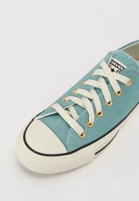 Light blue suede sneaker with white laces, gold eyelets, and a rubber toe cap. Features a black-striped outsole and brand label on tongue.