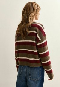 Pull rayé dans des tons marron, bordeaux et crème. Texture douce avec un col rond et une longueur cropped. Porté avec un jean bleu taille haute.