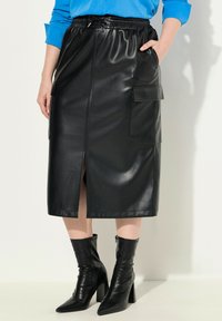 Gonna midi in eco-pelle nera con vita elastica, tasche laterali e spacco frontale. Indossata con stivaletti neri a punta e con tacco alto.