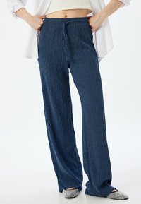 Blauwe, gestructureerde wijde broek met een elastische tailleband en trekkoord. Gecombineerd met versierde instapschoenen.