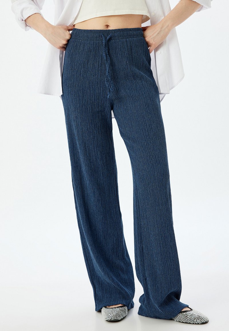 Blauwe, gestructureerde wijde broek met een elastische tailleband en trekkoord. Gecombineerd met versierde instapschoenen.