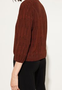 Løs, struktureret sweater i et rust- og sort zigzag-mønster. Har trekvartærmer og en rund halsudskæring.