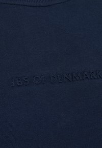Marineblå kortærmet skjorte lavet af blødt stof, med et struktureret præg logo "JES OF DENMARK" henover brystet.