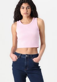 Svijetloružasti skraćeni top s rebrastom teksturom, okruglim izrezom i bez rukava, uparen s tamnoplavim trapericama visokog struka.