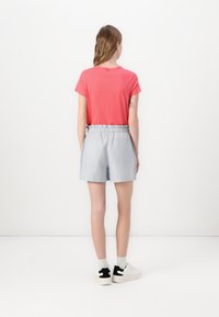 Red cotton t-shirt with short sleeves, paired with light gray shorts featuring a textured fabric and elastic waistband. White shoes with black accents.