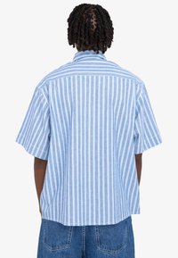 Camicia a maniche corte con bottoni di colore azzurro chiaro, con righe verticali bianche e rosa. Presenta un colletto classico e una vestibilità rilassata.