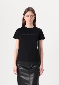 Juodas medvilninis marškinėliai su apvaliu kaklu ir trumpomis rankovėmis, su subtiliu iškilniu dizainu, kuriame užrašyta "KARL LAGERFELD". Šiek tiek laisvas fasonas.