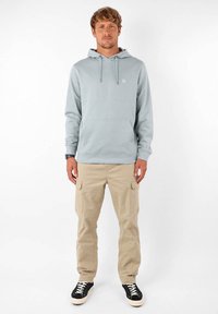 Sweat-shirt à capuche bleu clair avec une poche avant, associé à un pantalon cargo beige avec des poches latérales et des baskets montantes noires.
