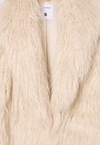 Cappotto in pelliccia sintetica di colore crema con una texture lunga e morbida. Presenta un semplice davanti aperto e un'etichetta che indica la taglia small.