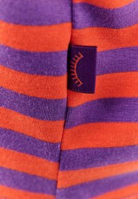 Skarpetki w paski z naprzemiennymi pomarańczowymi i fioletowymi kolorami, wykonane z miękkiej tkaniny, z małą fioletową metką z wzorem w krzywą linię.