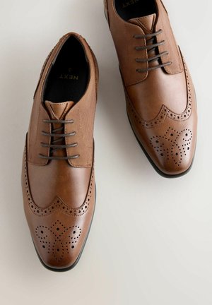 Ruske kožne brogue cipele s perforiranim detaljima, teksturiranom tkaninom na gornjem delu i ravnim vezicama. Dizajn s округlom nosom.