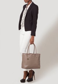 Taupe läderhandväska med dubbla handtag, texturerad yta och gulddetaljer. Har en dekorativ berlock.