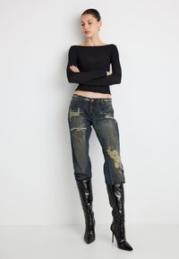 Top negru cu mâneci lungi și decolteu rotund, asortat cu blugi din denim uzat, cu accente cu ținte și pete, completat de cizme negre până la genunchi.