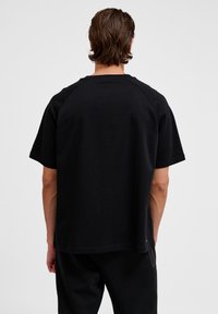 Svart kortärmad T-shirt med ribbad rund hals och raglanärmar, tillverkad av mjukt bomullstyg, visad från bakåtsidan.