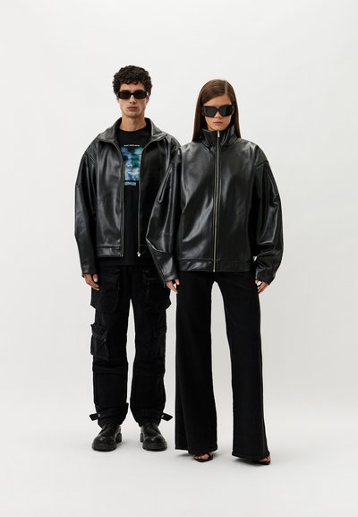Black leather zip-up jackets on two models, paired with a graphic tee and black cargo pants for one, wide-legged pants for the other.