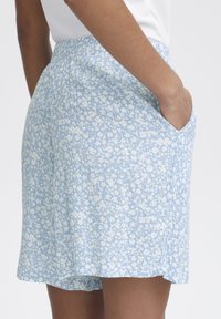 Ljusblå blommönstrad kortbyxa med texturerad tyg, elastisk midja och sidofickor. Sömmen faller strax över knäet.