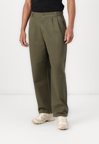 Olivengrønn, plisserte bukser laget av bomullsstoffblanding. Har en knappelukking, sidelommer og tapered ben-design.