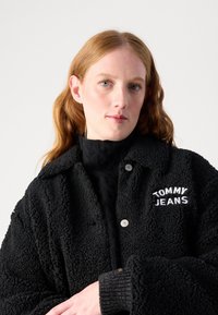 Veste en polaire noire et fluffy avec fermeture à boutons, col rabattu et logo brodé "TOMMY JEANS" sur la poitrine gauche. Détails des poignets côtelés.