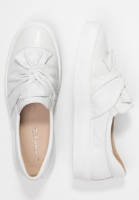 Baskets blanches en cuir avec un détail knoté à l'avant et des accents texturés, dotées d'une semelle en caoutchouc blanc plate et d'un intérieur lisse.