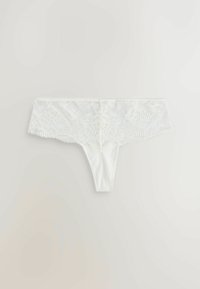 Fehér csipke tangapaplan virágmintával és fodros széllel, világos háttéren széthajtva.