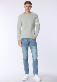 Maglione a maglia grigio chiaro con scollo rotondo e righe color crema sulle maniche, abbinato a jeans blu sbiaditi e sneakers bianche.